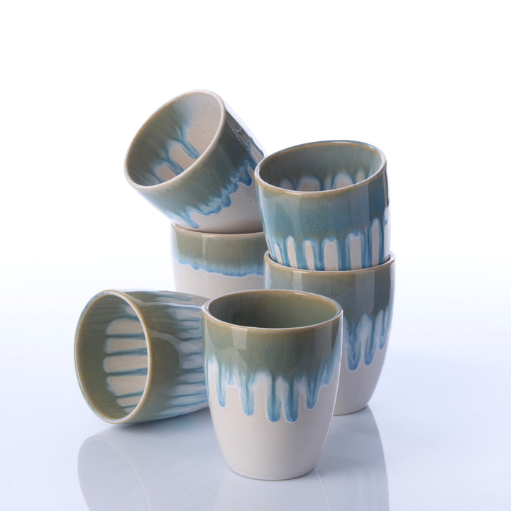 Sechs weiße Keramikbecher EBB &amp; FLOW blau aus unterschiedlichen Perspektiven mit fließendem blauem Glasurverlauf